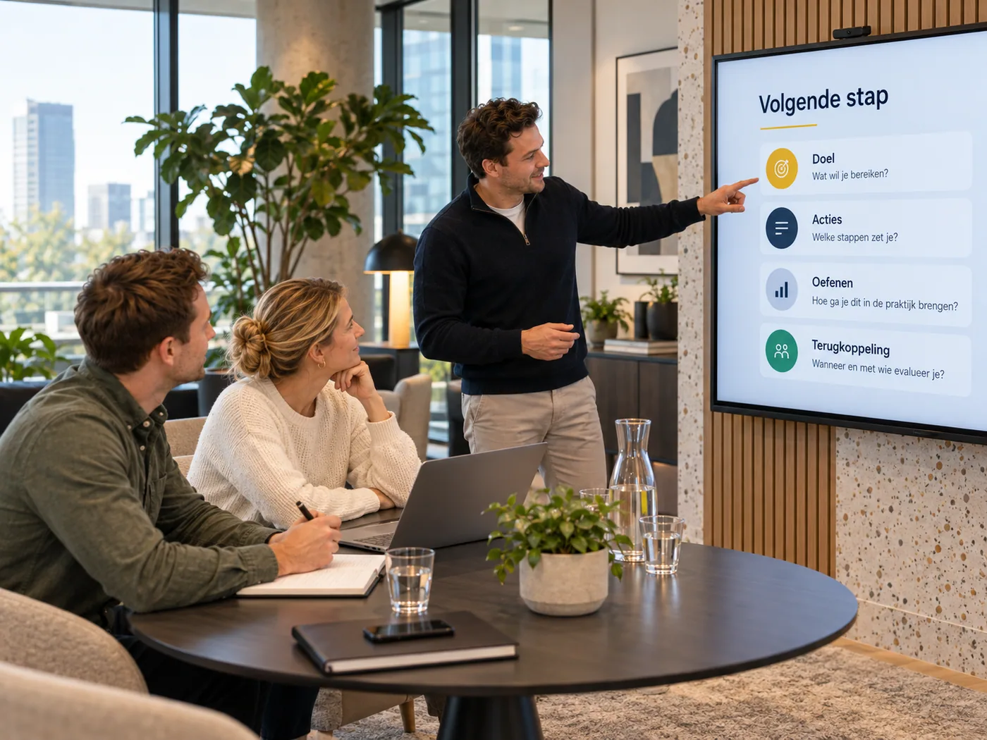 Een trainer wijst op het scherm met de volgende stap voor het team: doel, acties, oefenen en terugkoppeling.